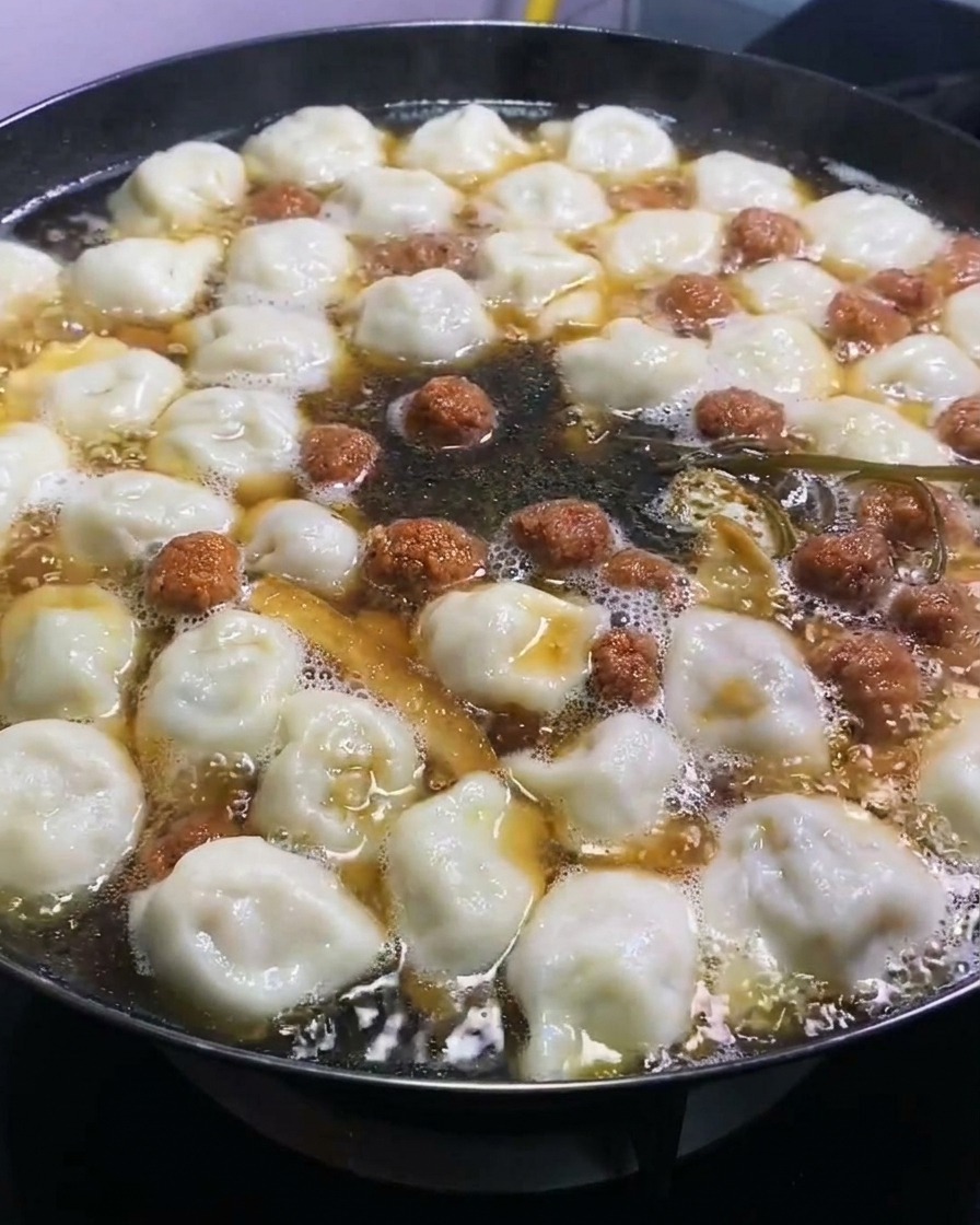 Salsa di soia scura aggiunta a una grande pentola di dumpling bollenti e ingredienti, aggiungendo un colore ricco.
