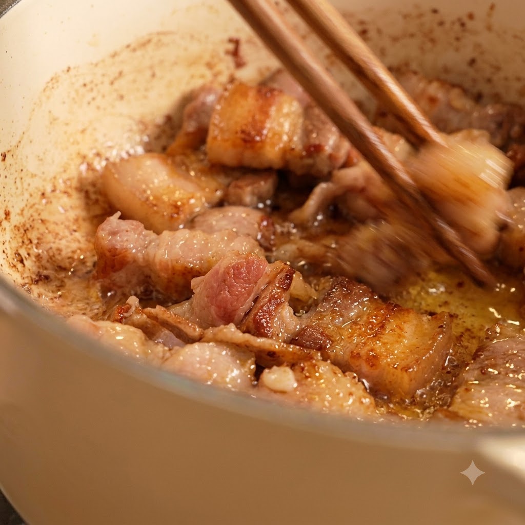 Bacchette che mescolano pezzi di carne rosolati che friggono nellolio dentro una pentola bianca.