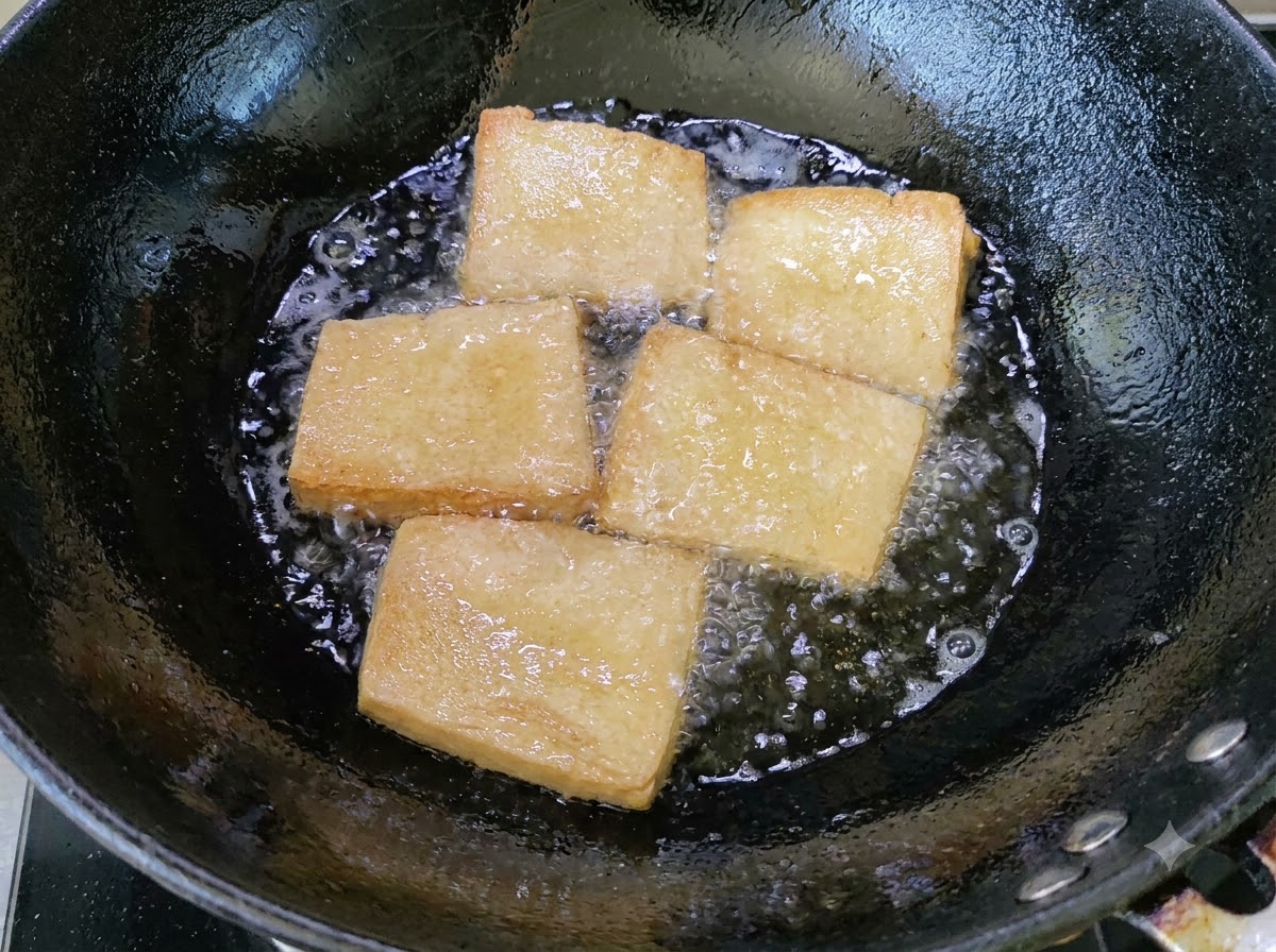 Pezzi di tofu dorati che friggono in un wok pieno di olio bollente.