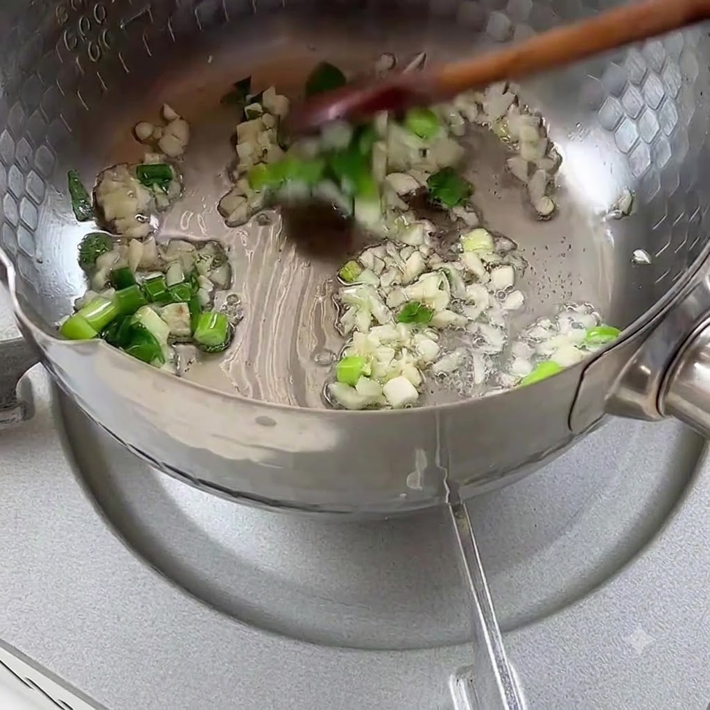 Cipollotti tritati e aglio sfrigolanti nellolio da cucina allinterno di una pentola di metallo.