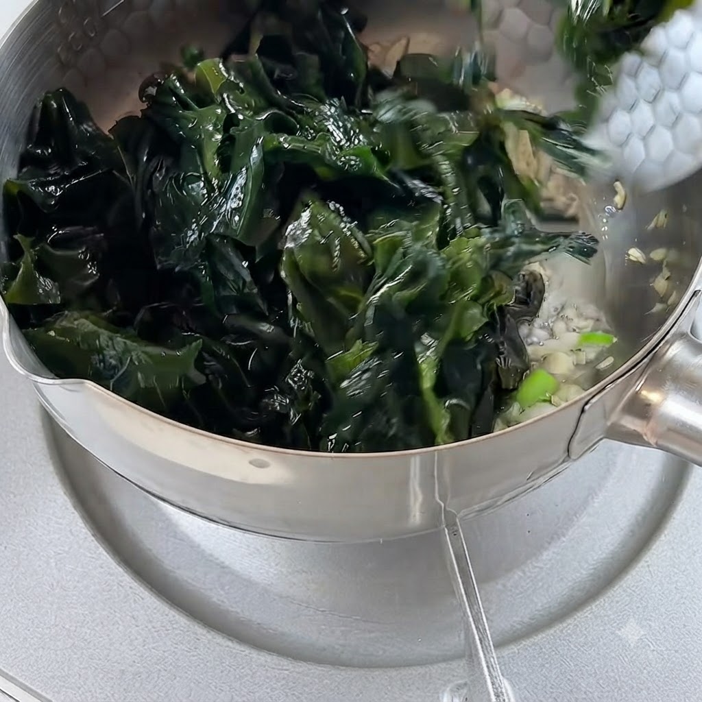 Alga reidratata aggiunta alla pentola contenente aglio e cipolle soffritti.