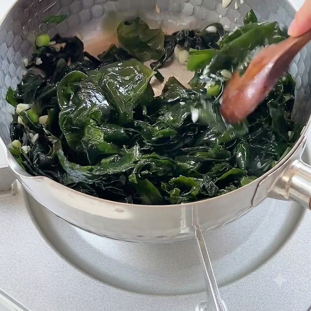 Acqua bollente versata in una pentola piena di alghe saltate e aromi.
