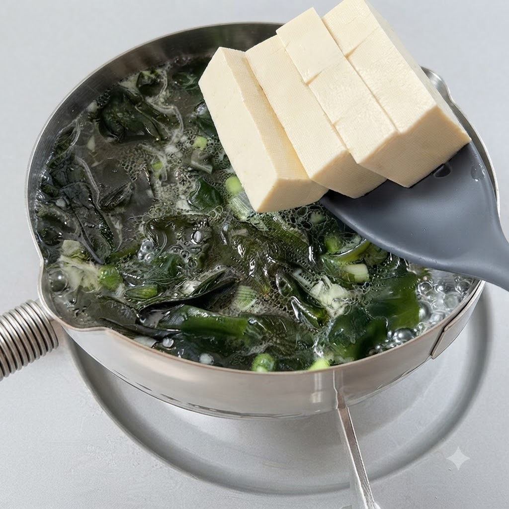 Cubetti di tofu trasferiti in una pentola bollente di zuppa di alghe usando un cucchiaio forato.
