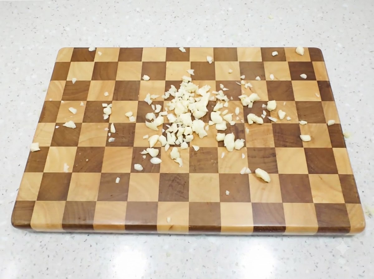 Spicchi daglio tritati finemente sparsi su un tagliere di legno a quadri.