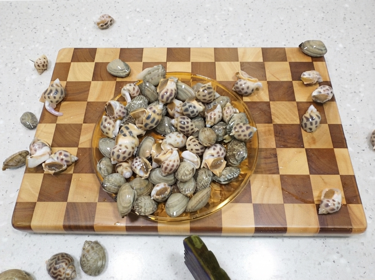 Un piatto pieno di lumache di mare maculate crude adagiate su un tagliere di legno.