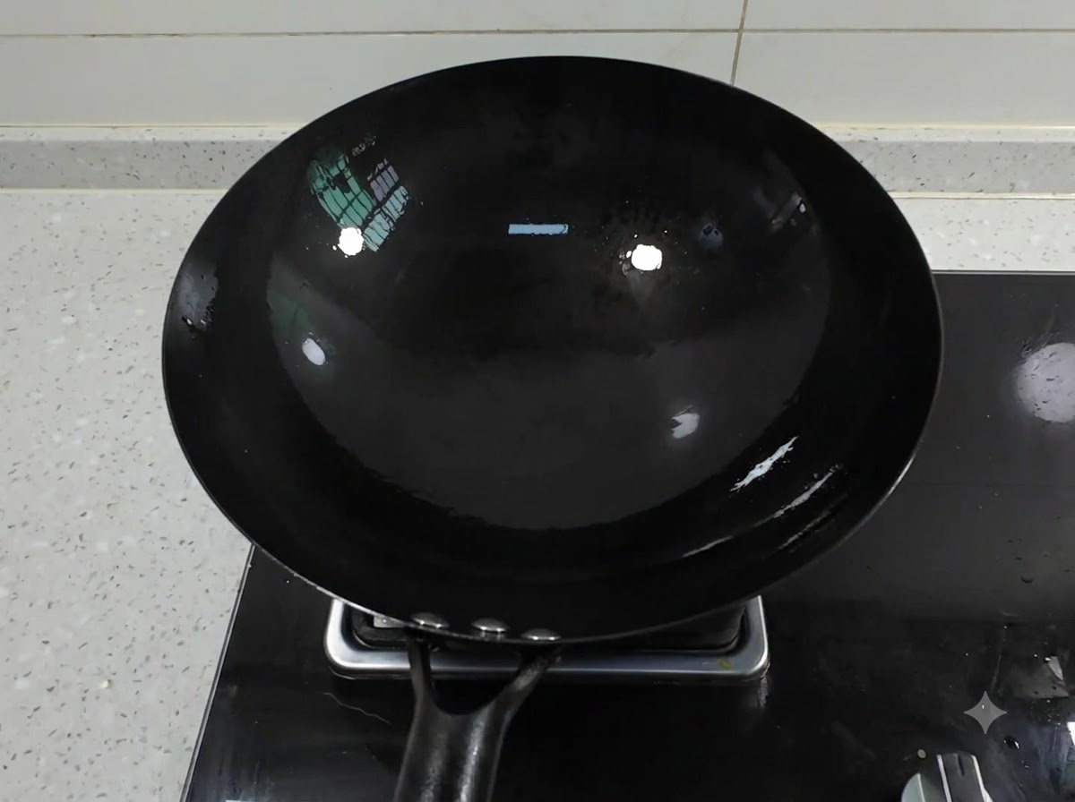 Un pulito wok di ferro nero posizionato su un fuoco a gas con olio che si raccoglie allinterno.
