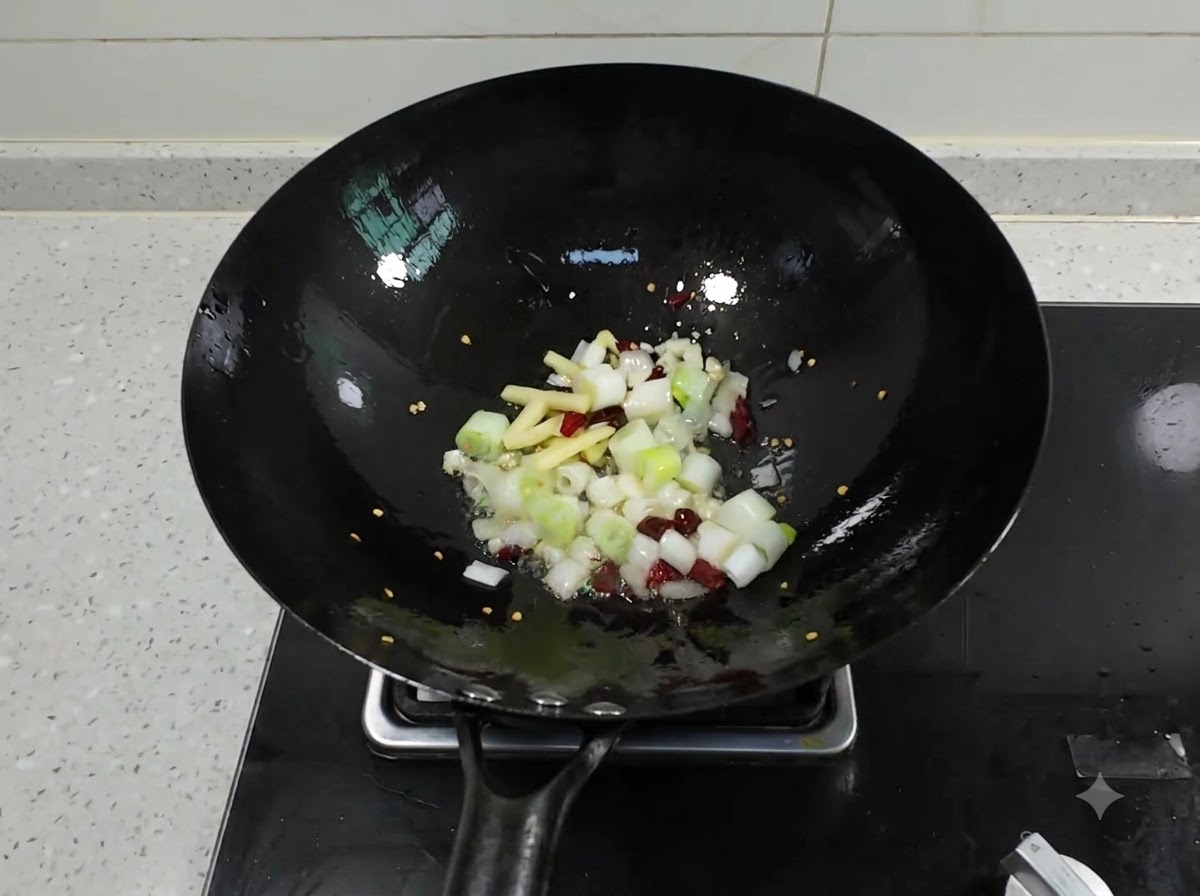 Cipollotti tritati, zenzero, aglio e peperoncini secchi che sfrigolano in un wok nero con olio caldo.