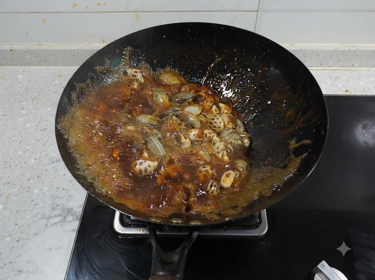 Lumache di mare e polipetti che sobbollono in un brodo rosso piccante scuro che bolle vigorosamente dentro un wok nero.