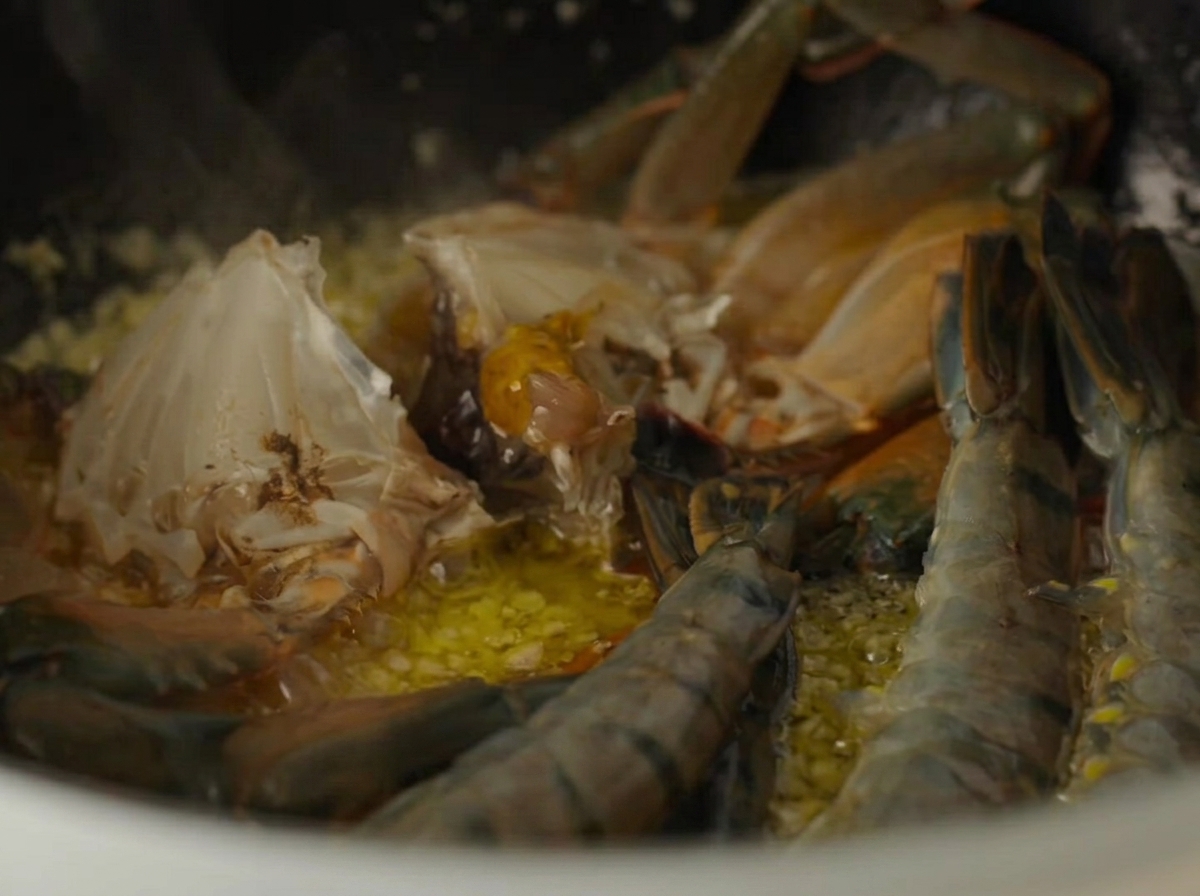 Pezzi di granchio crudo e gamberi crudi che cuociono allinterno di una pentola con burro allaglio.