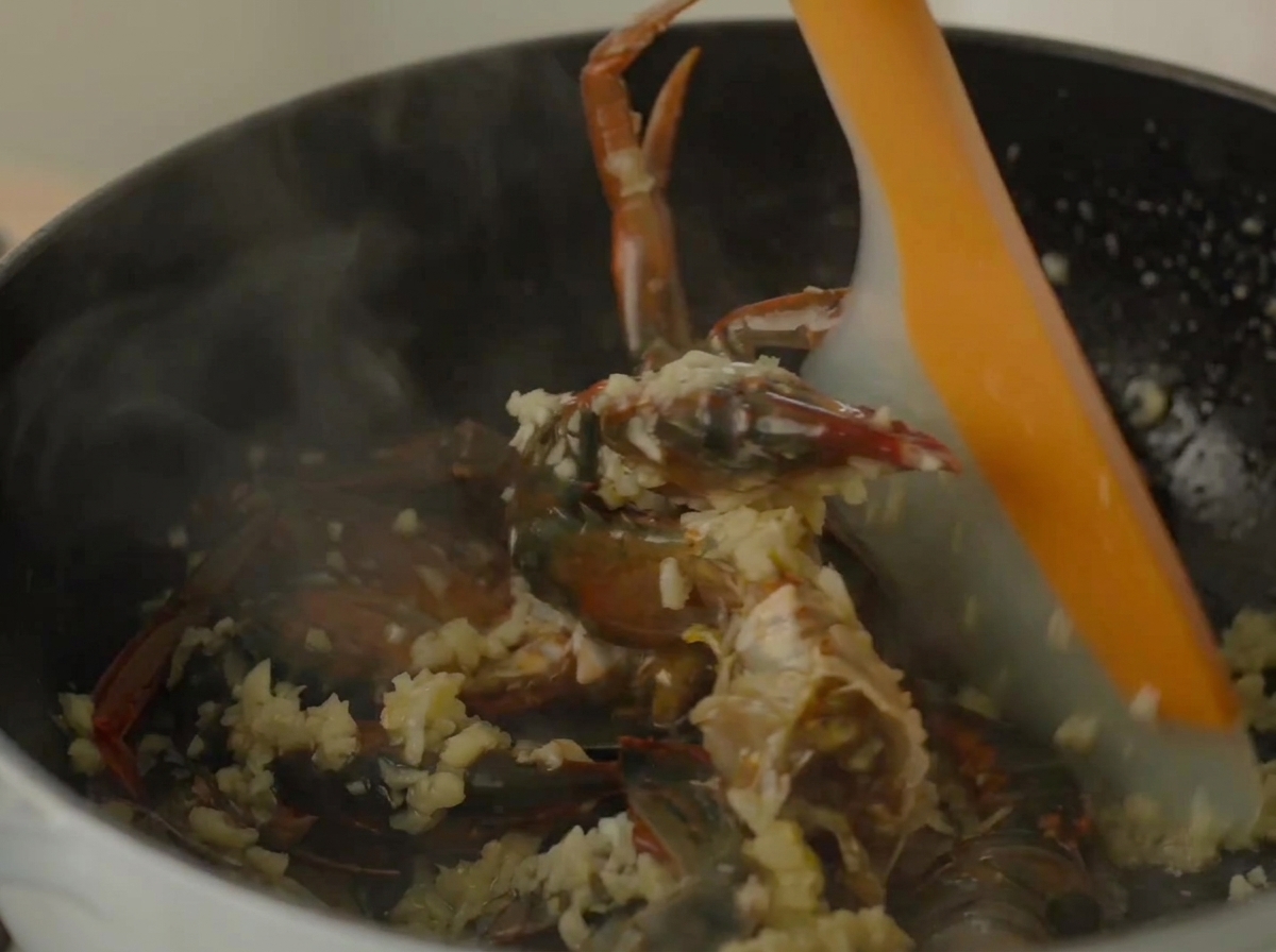 Una spatola in silicone che mescola granchio e gamberi allinterno di una pentola fumante.
