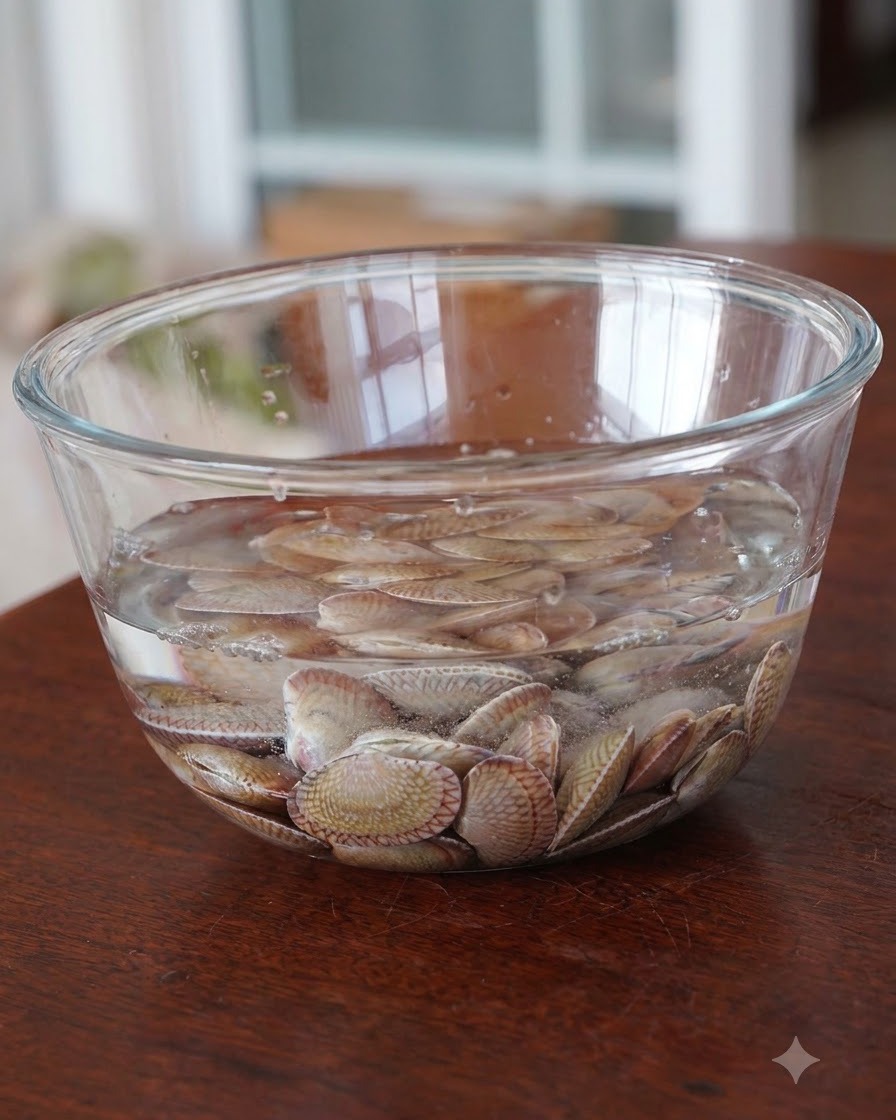 Vongole fresche crude in ammollo in una ciotola di vetro trasparente riempita dacqua.