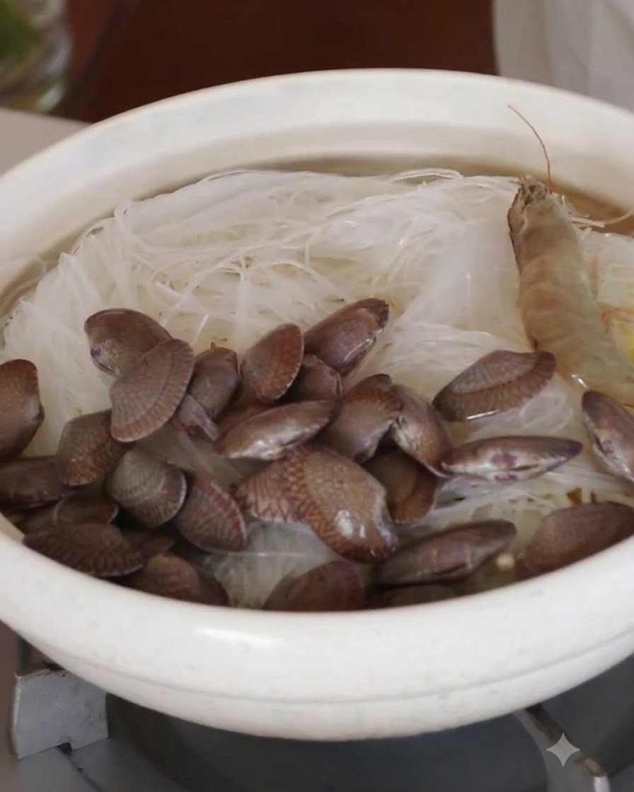 Gamberi interi crudi e vongole fresche disposti in cerchio sopra i noodles di vetro.