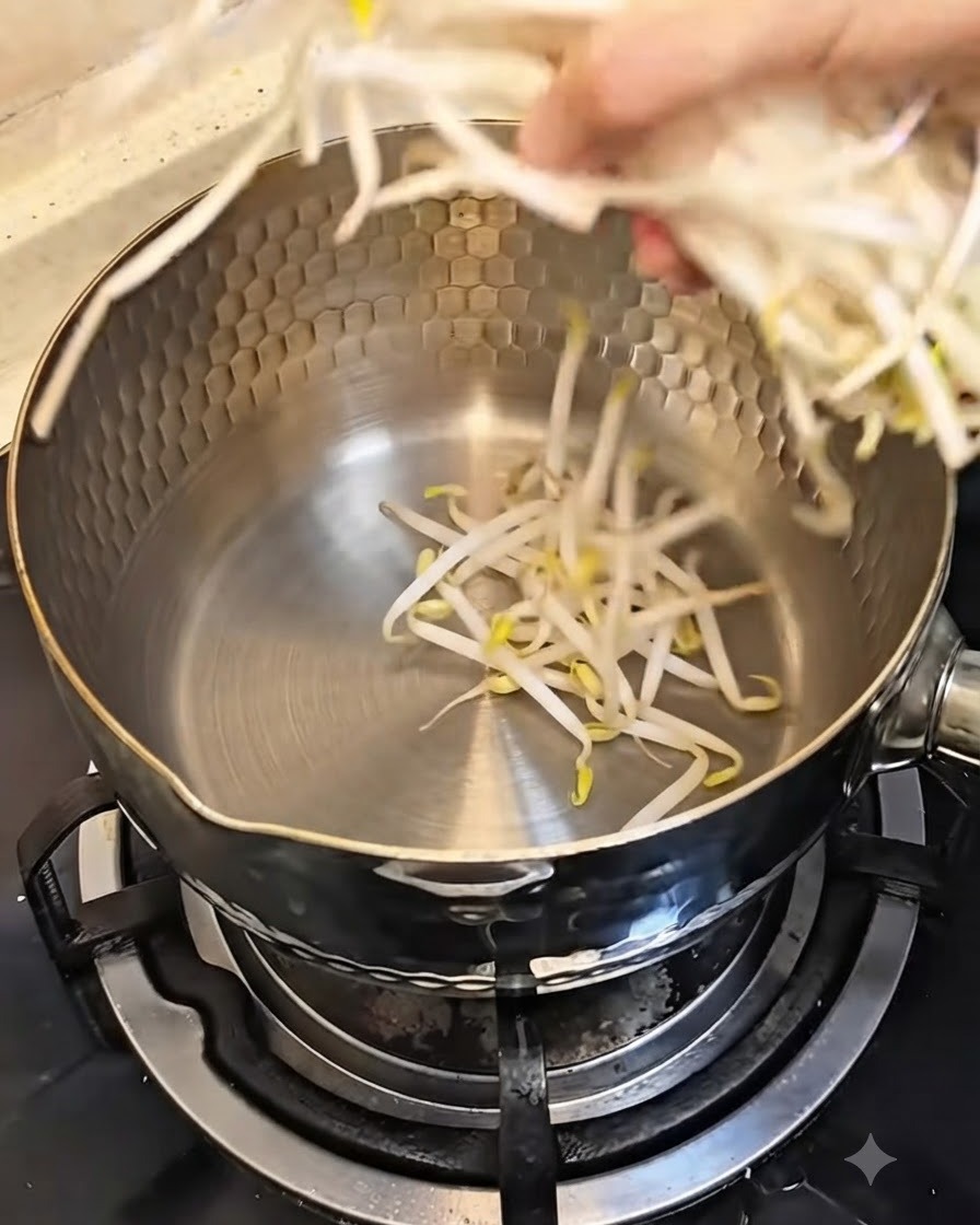 Una mano che mette una manciata di germogli di soia freschi in una pentola di metallo pulita.