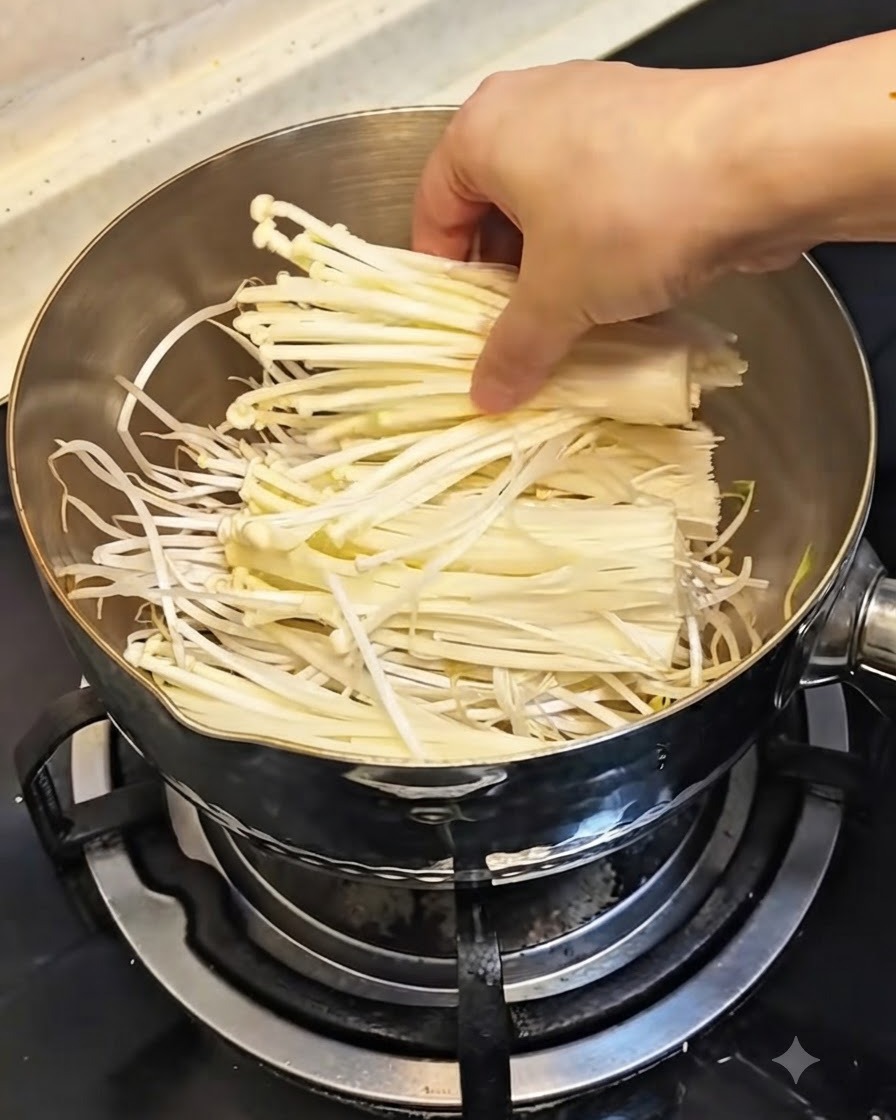 Una mano che posiziona un mazzetto di funghi enoki bianchi freschi sopra i germogli di soia nella pentola.