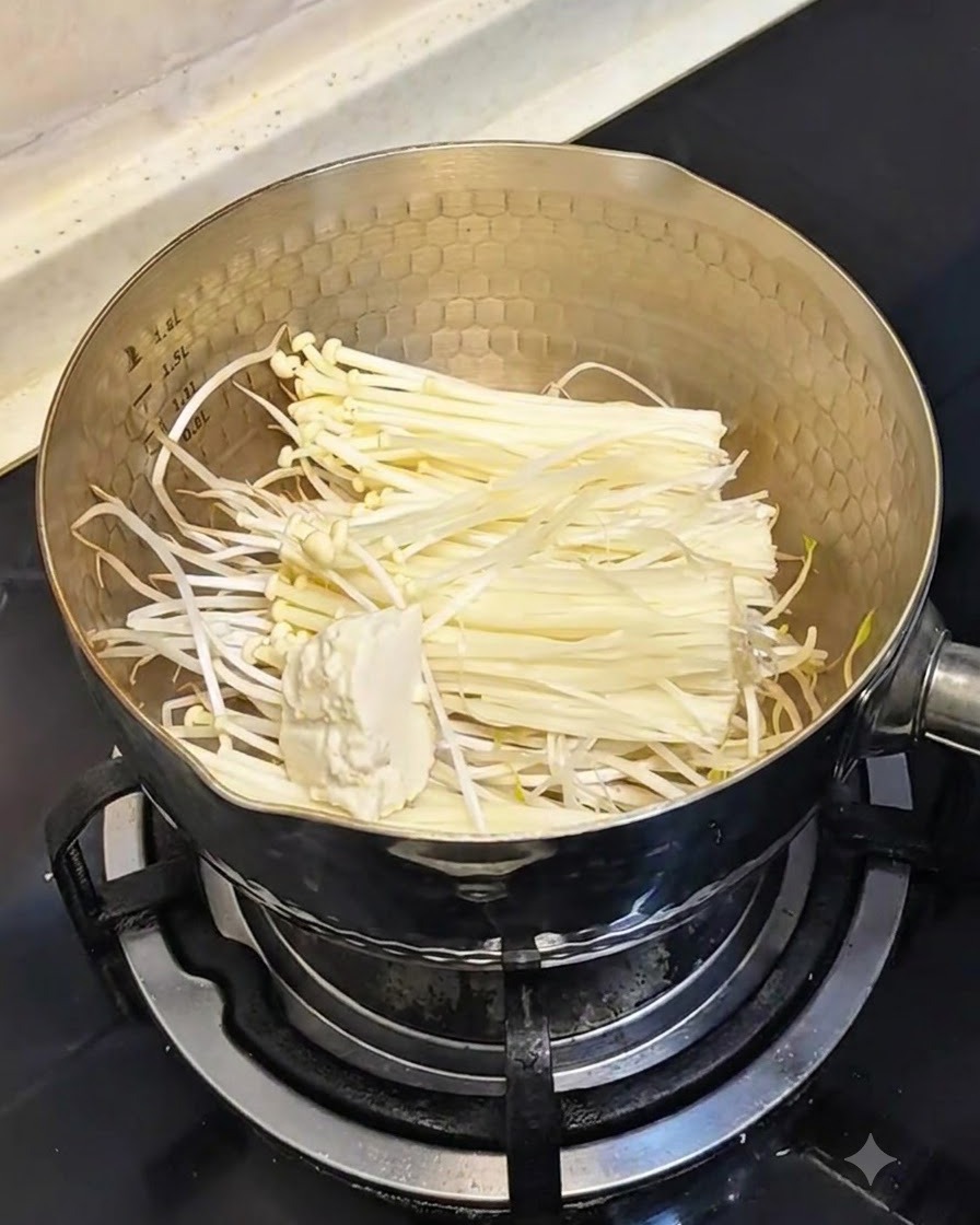 Un cucchiaio di tofu vellutato morbido aggiunto nella pentola contenente germogli di soia e funghi.