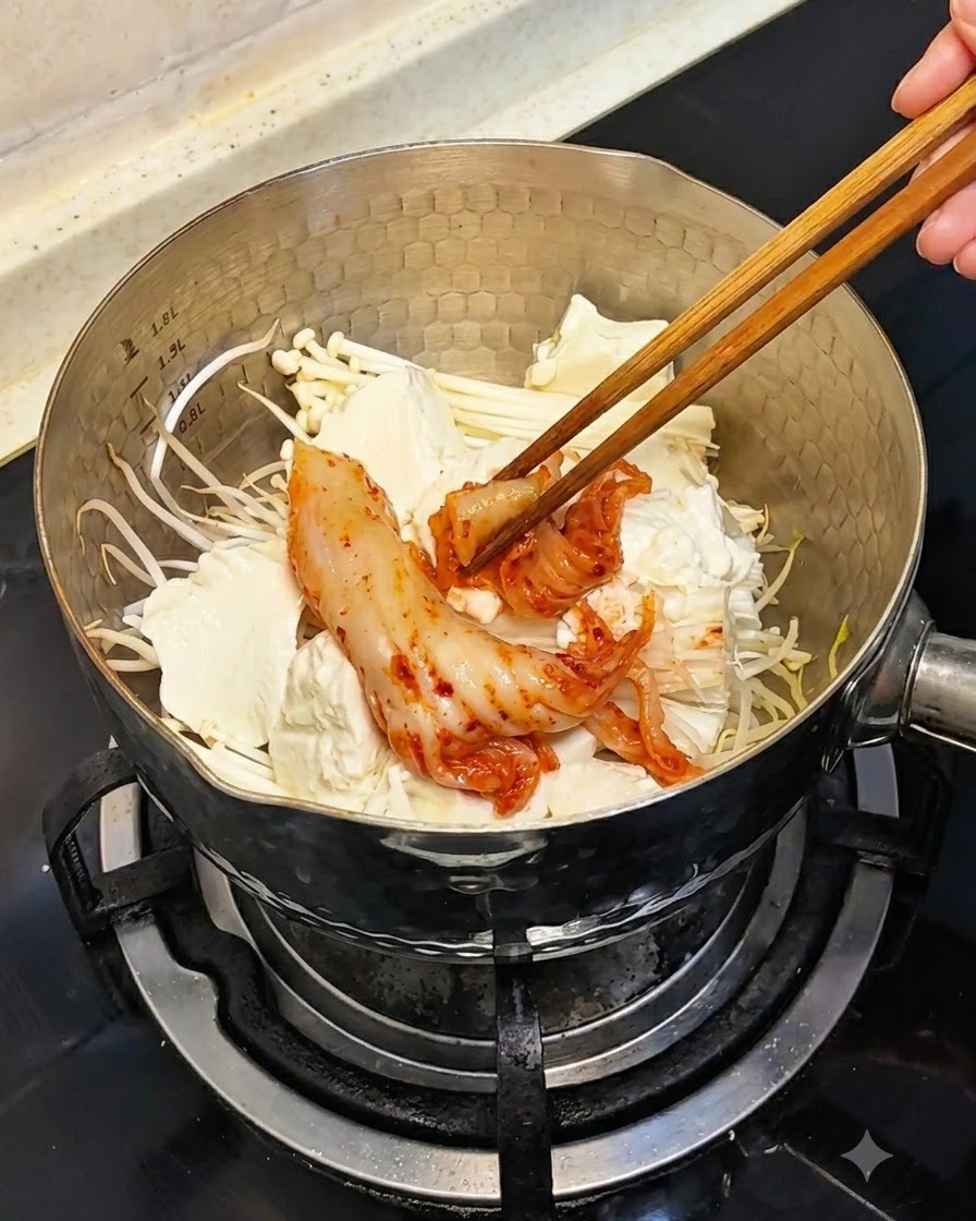 Le bacchette che mettono pezzi di kimchi rosso fermentato nella pentola sopra il tofu e i funghi.