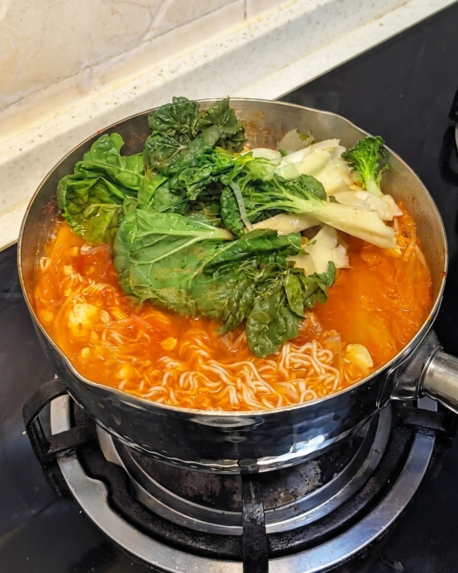Verdure a foglia verde fresche aggiunte sopra gli ingredienti bollenti nella pentola.