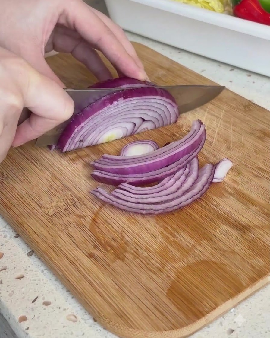 Mezza cipolla rossa tagliata a strisce sottili su un tagliere di legno.
