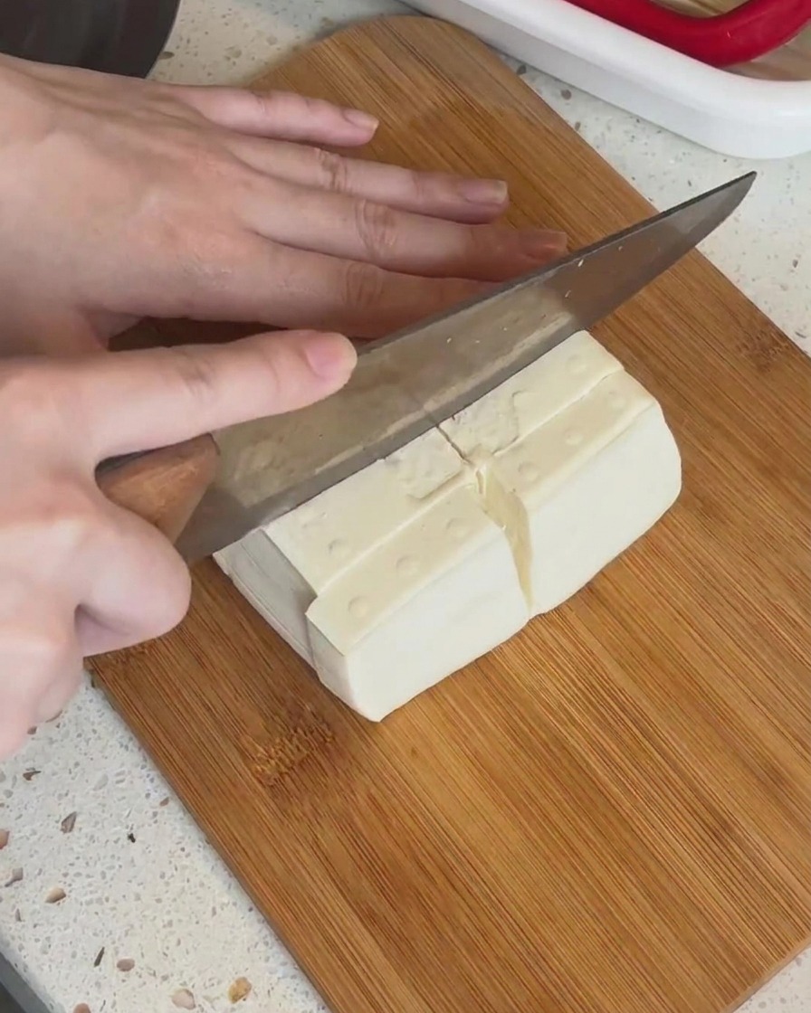 Un panetto di tofu bianco tagliato a piccoli pezzi rettangolari su un tagliere di legno.