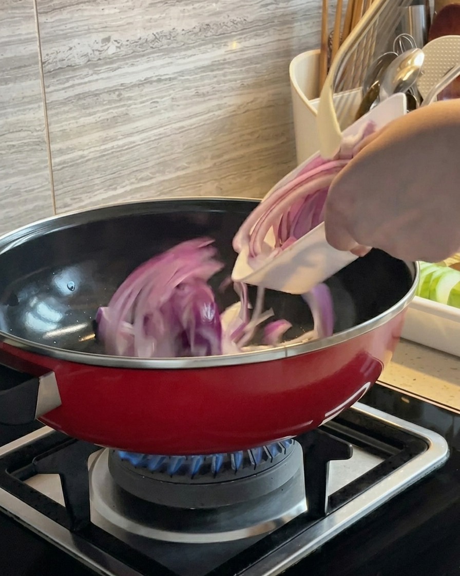 Fette di cipolla rossa saltate in padella in una pentola rossa su un fornello a gas.