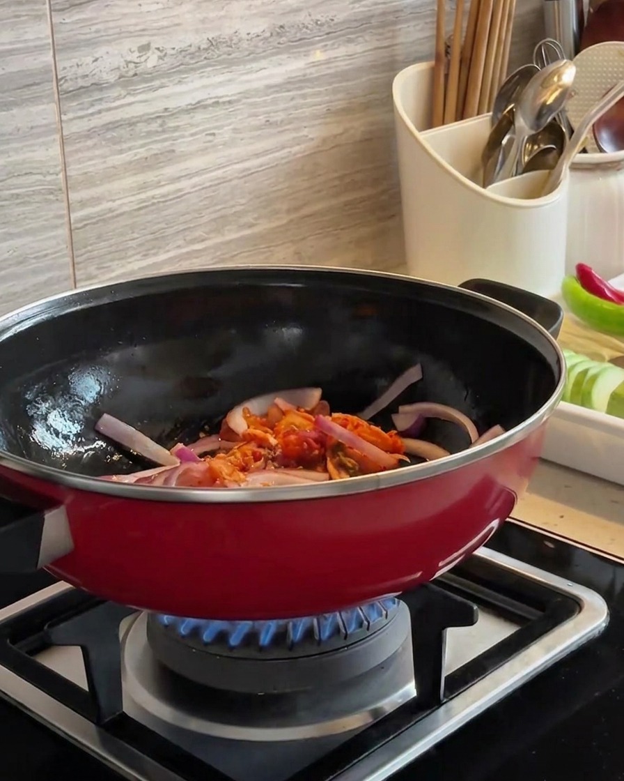 Cipolle rosse a fette e kimchi tritato saltati insieme in un wok rosso su una fiamma blu.
