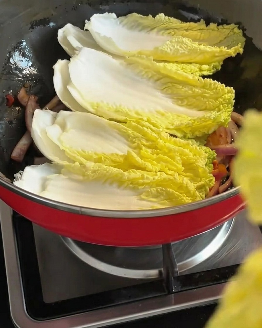 Foglie fresche di cavolo napa adagiate sulla miscela di cipolle e kimchi saltati in padella.