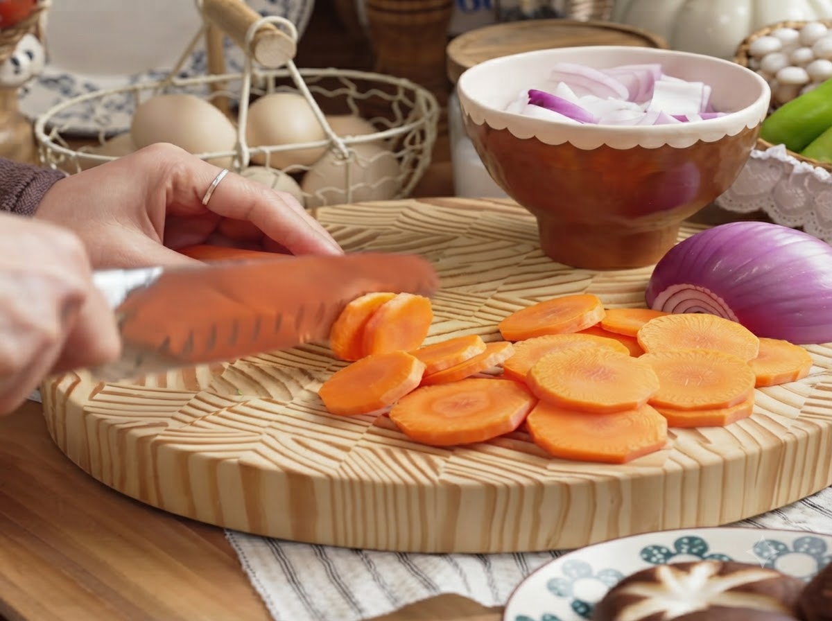 Una mano che affetta una carota pelata a rondelle su un tagliere di legno.