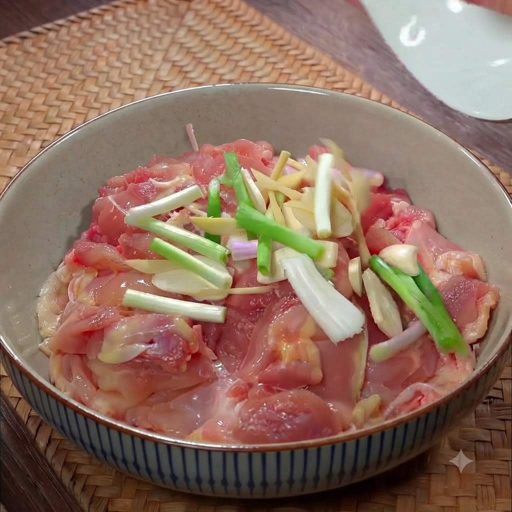 Pezzi di pollo crudo in una ciotola di ceramica guarniti con scalogni affettati, julienne di zenzero e pezzi daglio.