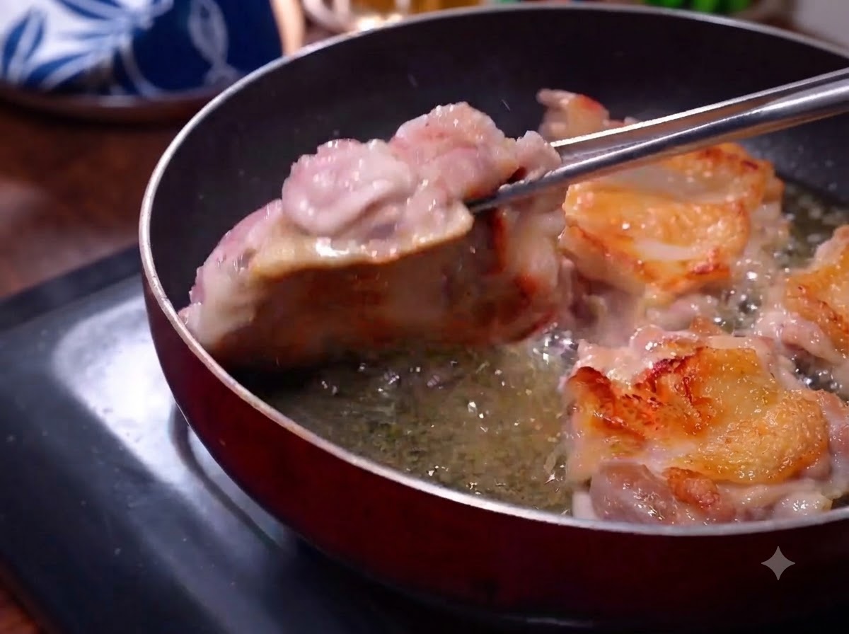 Cosce di pollo che friggono in una padella con la pelle dorata visibile mentre le pinze le girano.