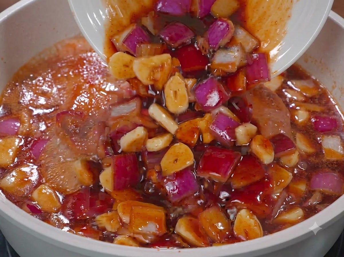 Salsa e cipolle rosse versate da un piatto bianco in una padella con il pollo.