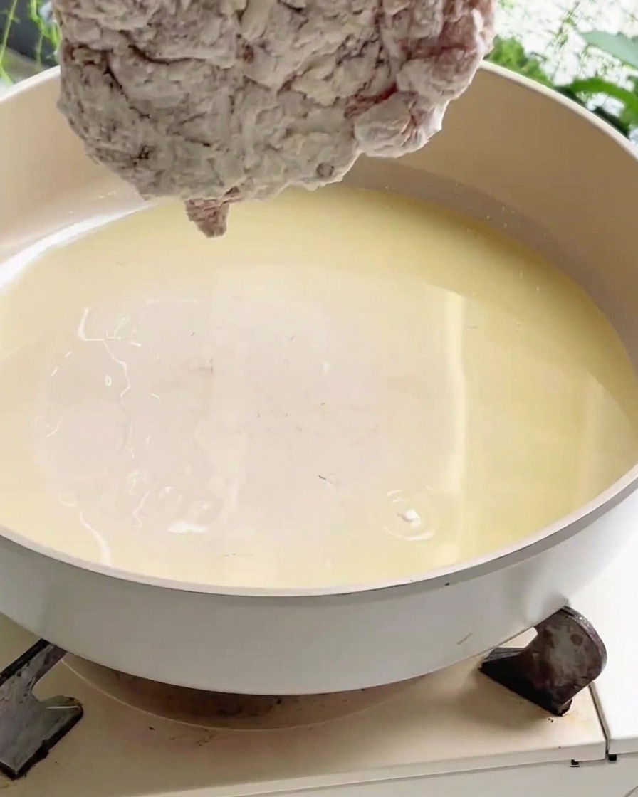 Un pezzo di pollo infarinato che viene immerso in unampia padella piena di olio da cucina caldo su un fornello.