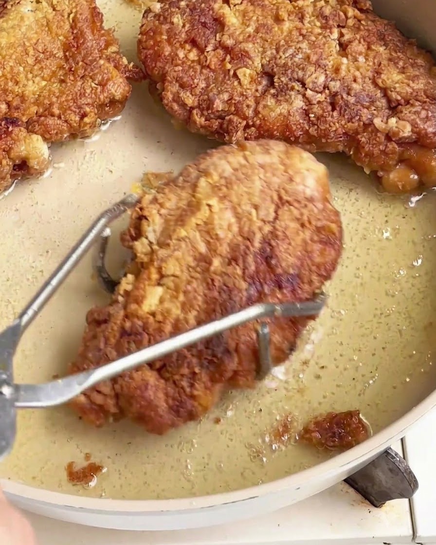 Cotolette di pollo fritte croccanti sollevate da una padella oleosa usando pinze in acciaio inossidabile.