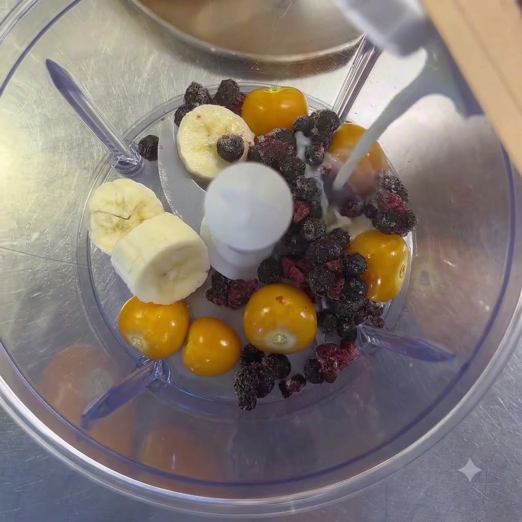 Il latte che viene versato da un cartone in un frullatore riempito con uva spina, fette di banana e frutti di bosco misti.