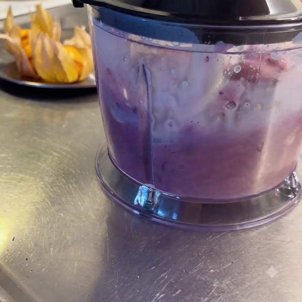 Un frullatore in funzione che lavora frutti di bosco misti, frutta e latte trasformandoli in un frullato viola liscio.