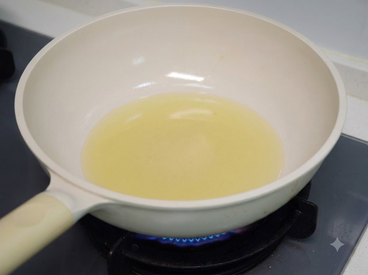 Olio da cucina che si scalda in una padella bianca su un fornello a gas.