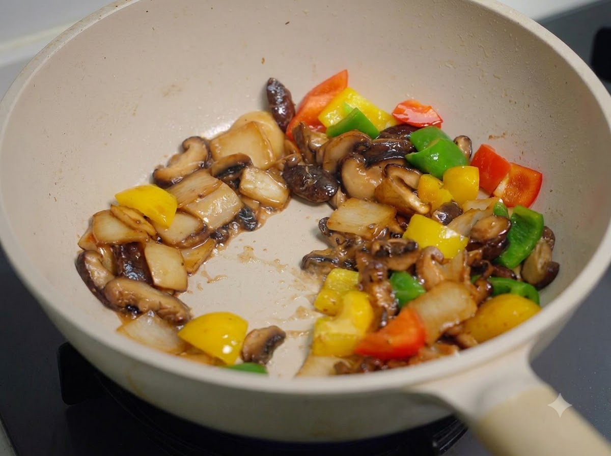Tutti i funghi e i peperoni saltati e mescolati rapidamente nella padella, rivestiti uniformemente da una spessa salsa scura.