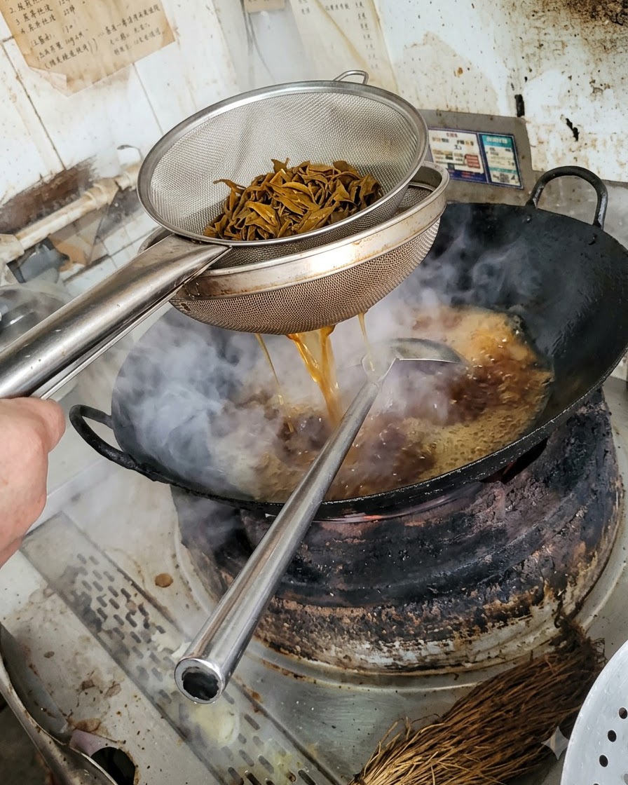 Uno scolapasta di metallo che contiene strisce di funghi scure sbollentate, con il liquido che drena nel wok sottostante.