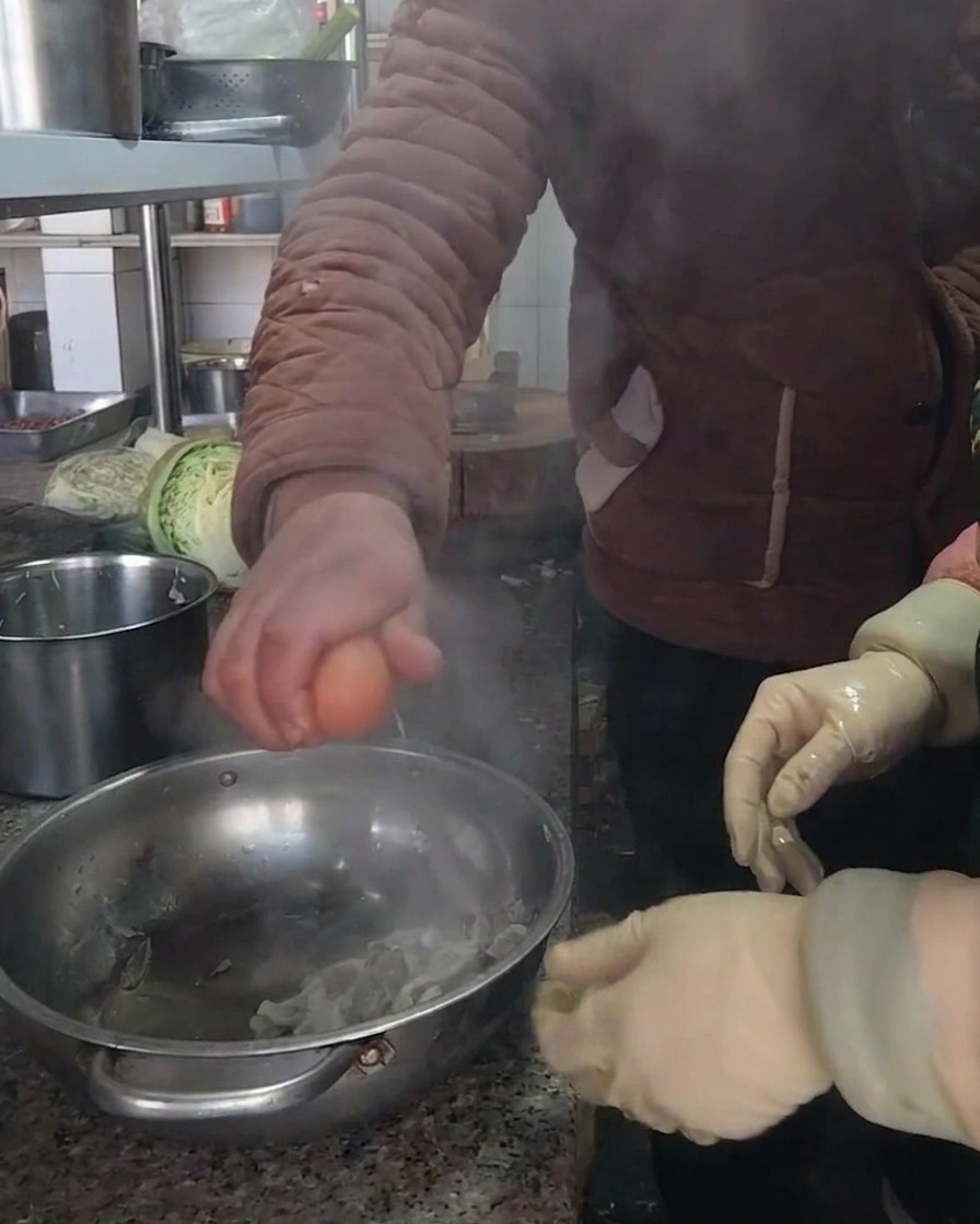 Una persona che rompe un uovo marrone fresco in una ciotola di acciaio inossidabile contenente i funghi preparati.