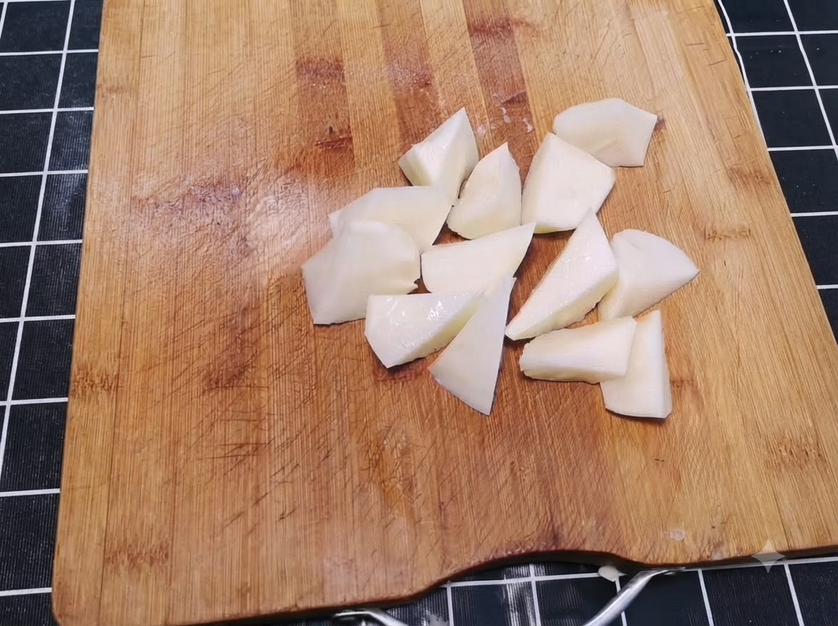 Patate pelate tagliate a pezzi irregolari grandi un boccone sparse su un tagliere di legno.
