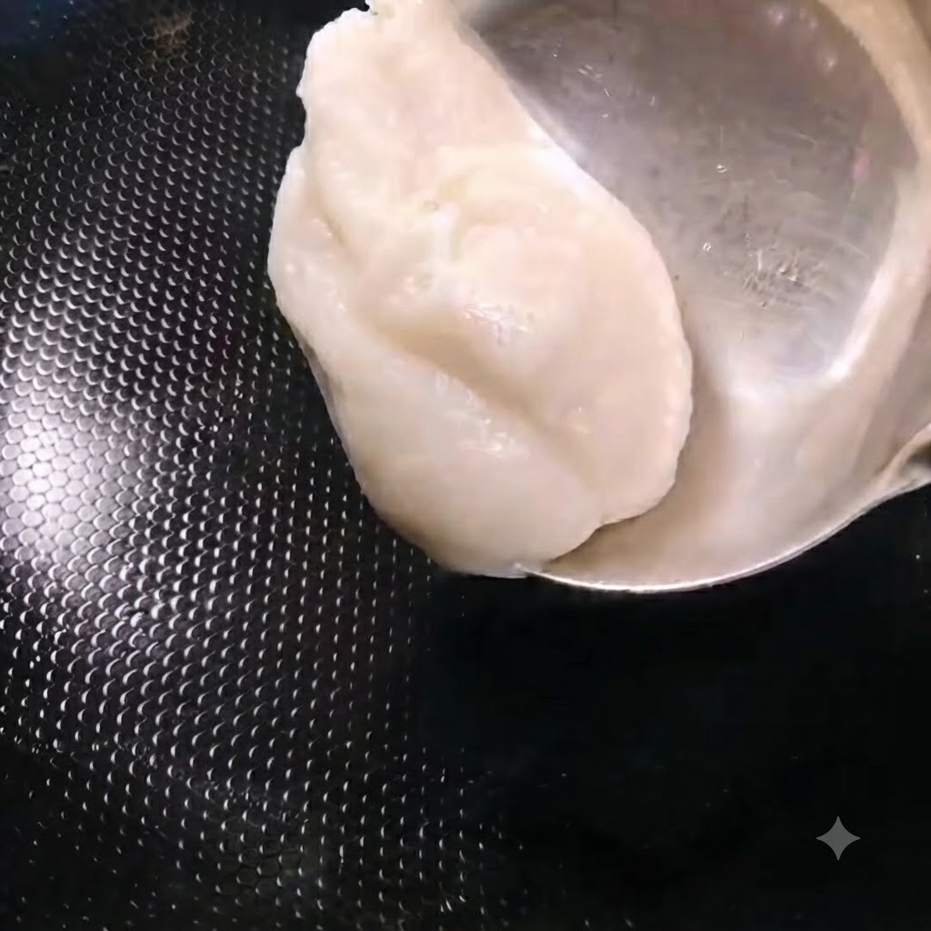 Un mestolo che aggiunge un cucchiaio di strutto di maiale bianco in un wok nero riscaldato.