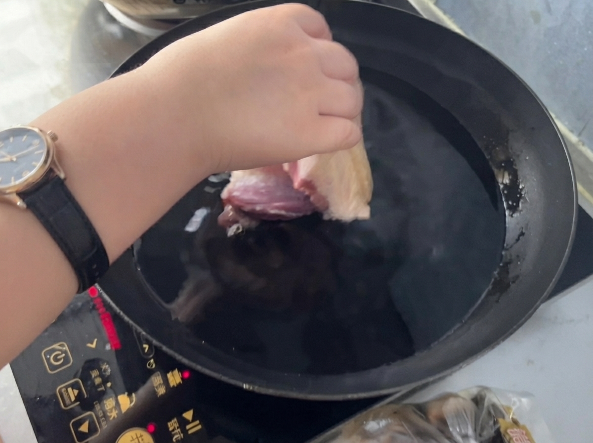 Una mano che inserisce un pezzo di maiale in una padella di acqua fredda con zenzero e vino da cucina.