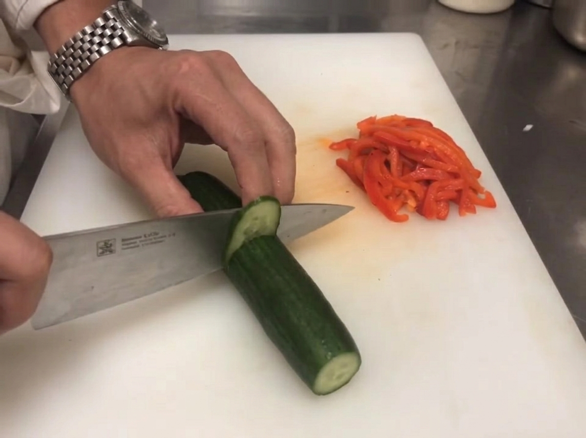 Un coltello che taglia un cetriolo verde fresco vicino a peperoni rossi affettati.