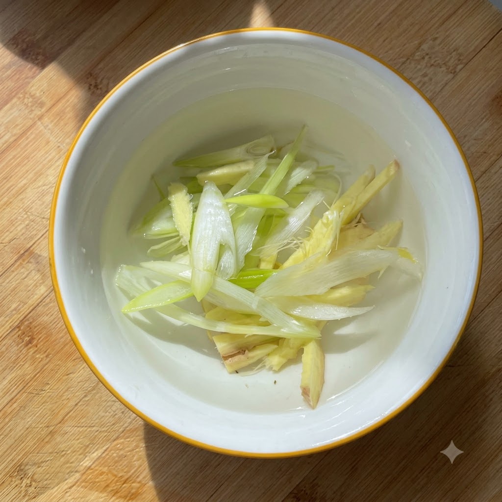 Cipollotti affettati e pezzi di zenzero in infusione nellacqua allinterno di una piccola ciotola bianca.