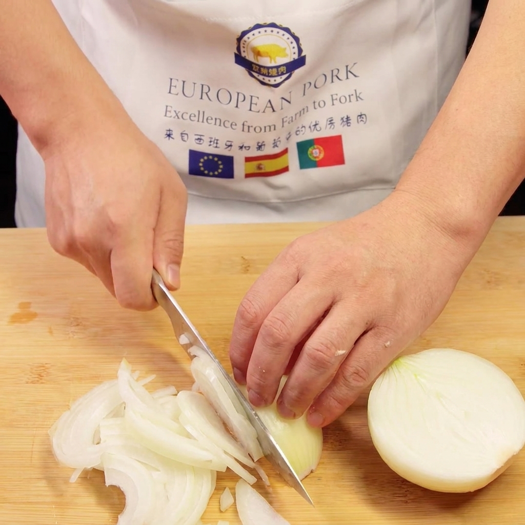 Le mani di uno chef che affettano una cipolla in listarelle sottili su un tagliere di legno.