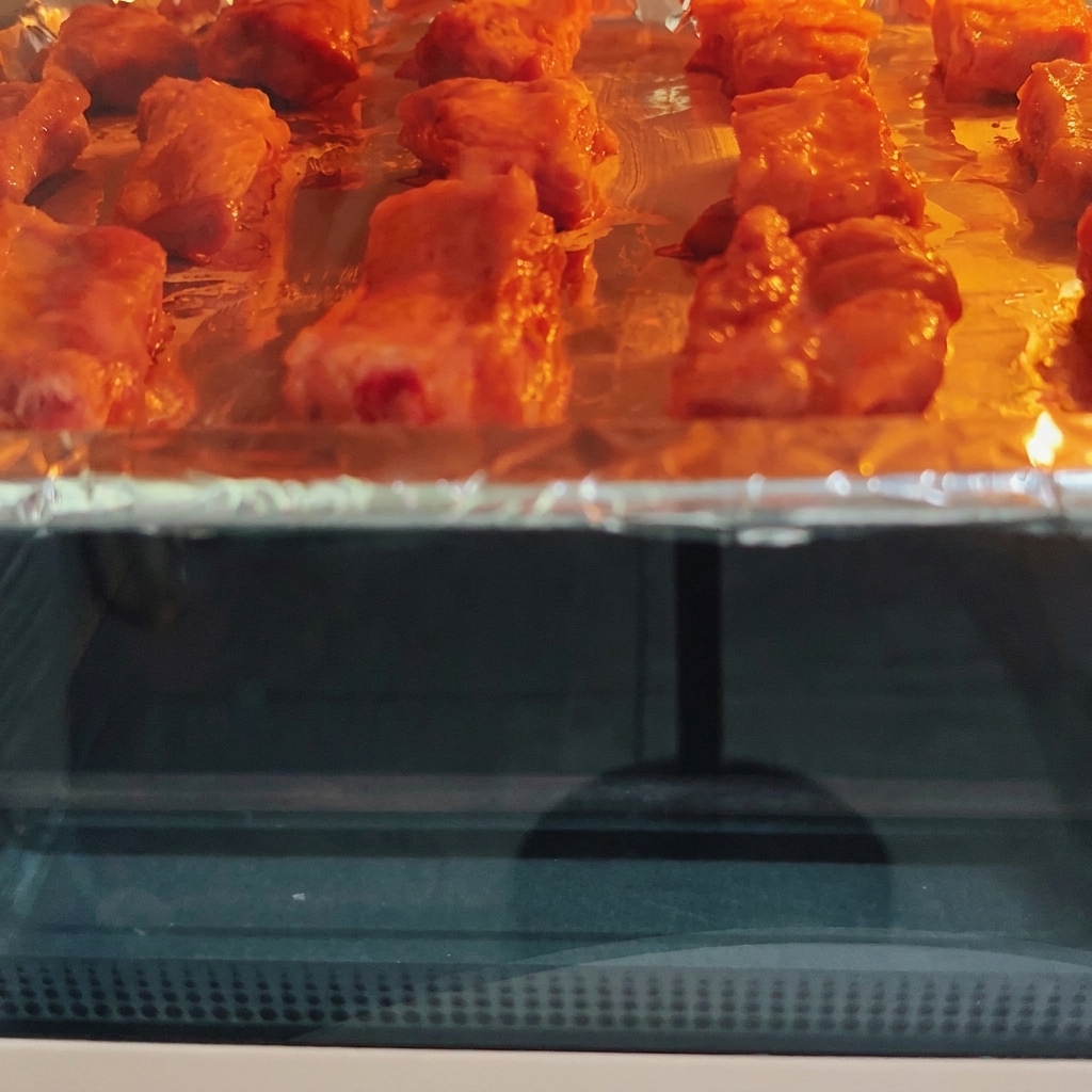 Costine di maiale in cottura allinterno di un forno caldo su una teglia, che mostrano una doratura visibile sotto lelemento riscaldante.