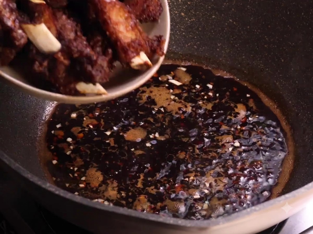 Costine di maiale fritte trasferite da un piatto nella salsa scura che sobbolle in un wok.