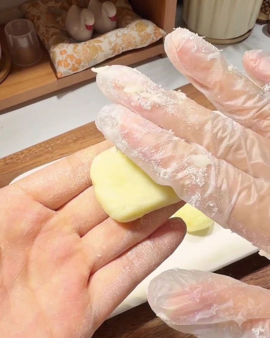 Una mano guantata che preme una piccola pallina di impasto di patate per formare un pancake piatto e rotondo nel palmo della mano.