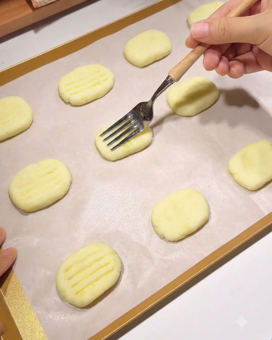 Una forchetta con manico di legno che preme un motivo di linee parallele in un pancake di patate modellato su una teglia foderata di carta da forno.