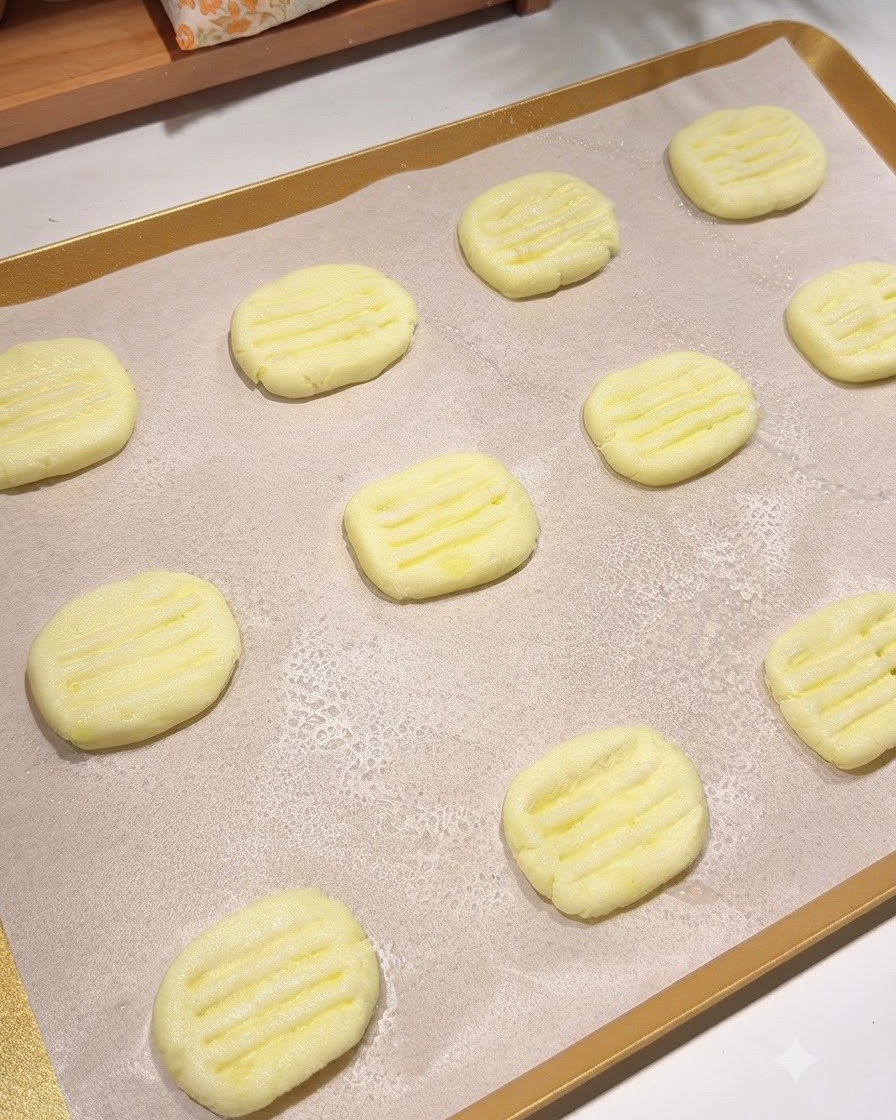 Una teglia foderata di carta da forno contenente più pancake di patate sagomati con un sottile strato di olio da cucina spruzzato sopra.