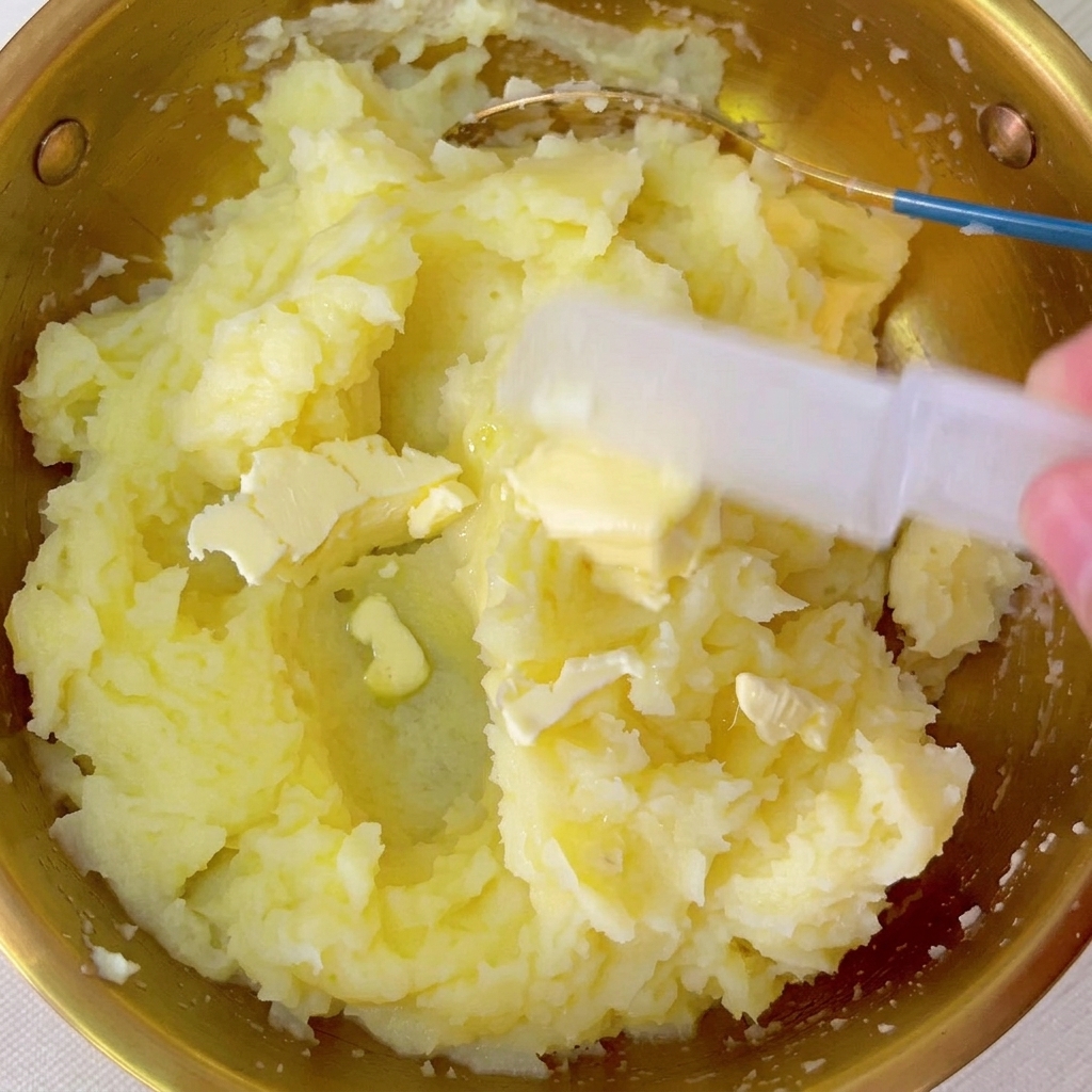 Pecche di burro mescolate nella ciotola di purè di patate tiepido.